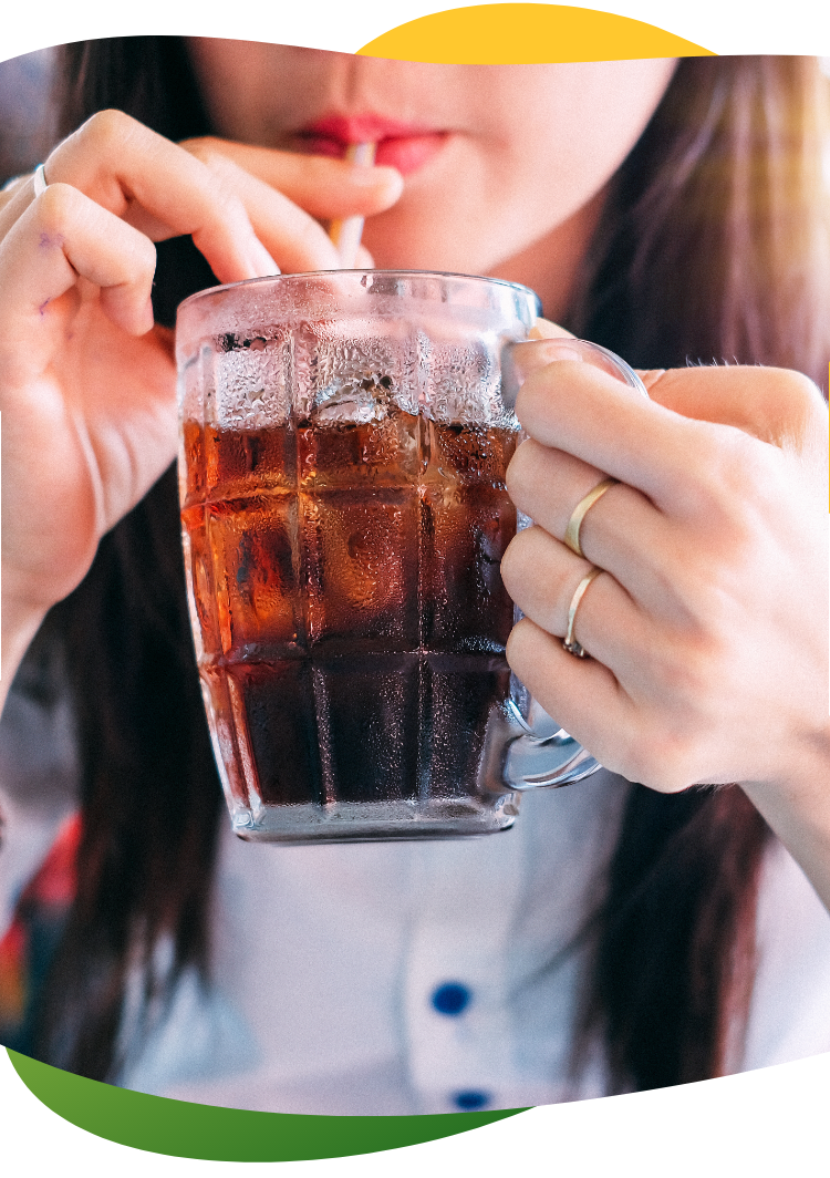 Mladá žena s dlhými hnedými vlasmi drží v ruke vysoký pohár a pije z neho slamkou sýtený nápoj slamkou.