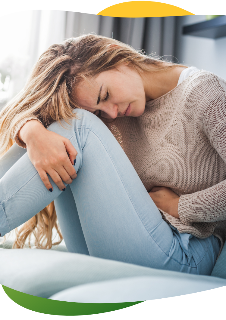 Mladá žena trpí menštruačným nadúvaním, sedí v kŕčoch na podlahe a ľavou rukou si drží brucho.